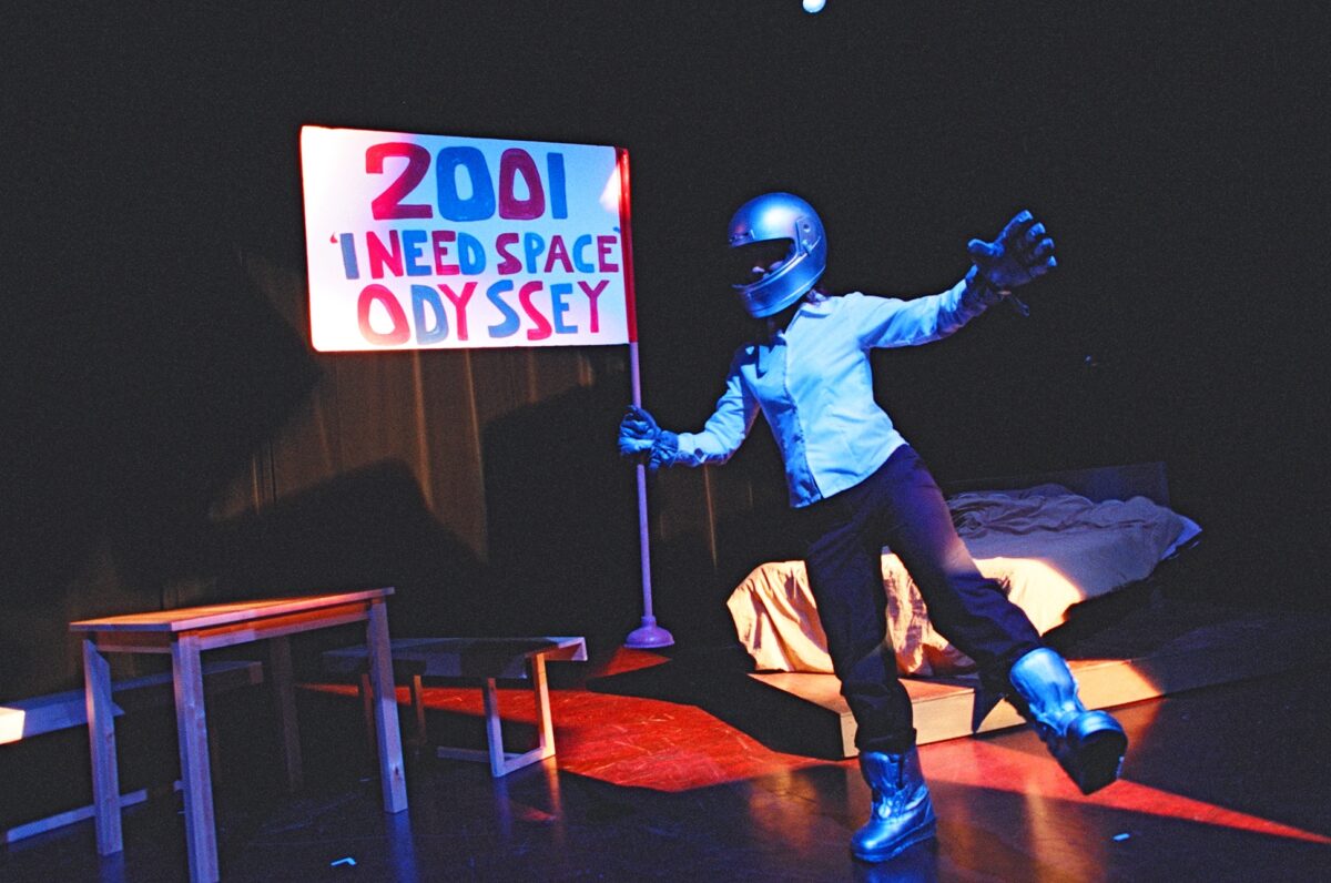 Men of the World. Celebrated 20 years in 2020. The image for 2004 shows a spaceman holding a sign that reads, "2001 I Need Space Odyssey" on a stage with a table, chair and mattress on the floor behind him.