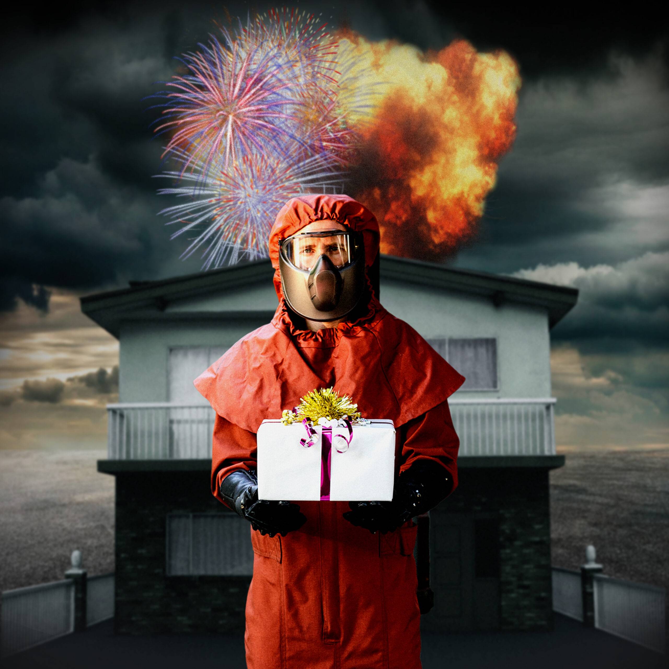 A person in a red hazmat suit holding a present which is a box with a ribbon and a bow. Behind him are a house and stormy clouds and light, fireworks, and fire