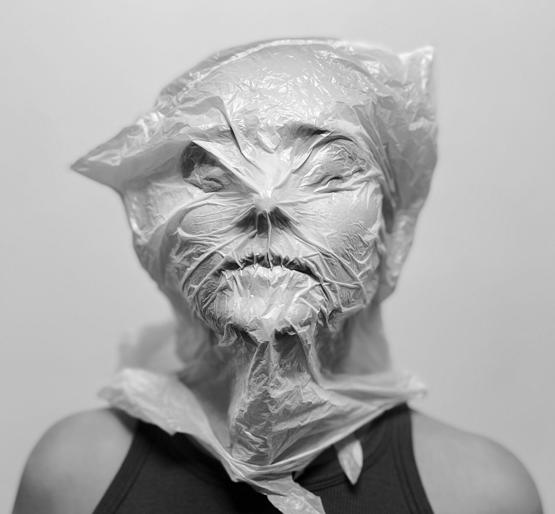 A woman wearing a black shirt breathes in a plastic bag over her head. She is calm.