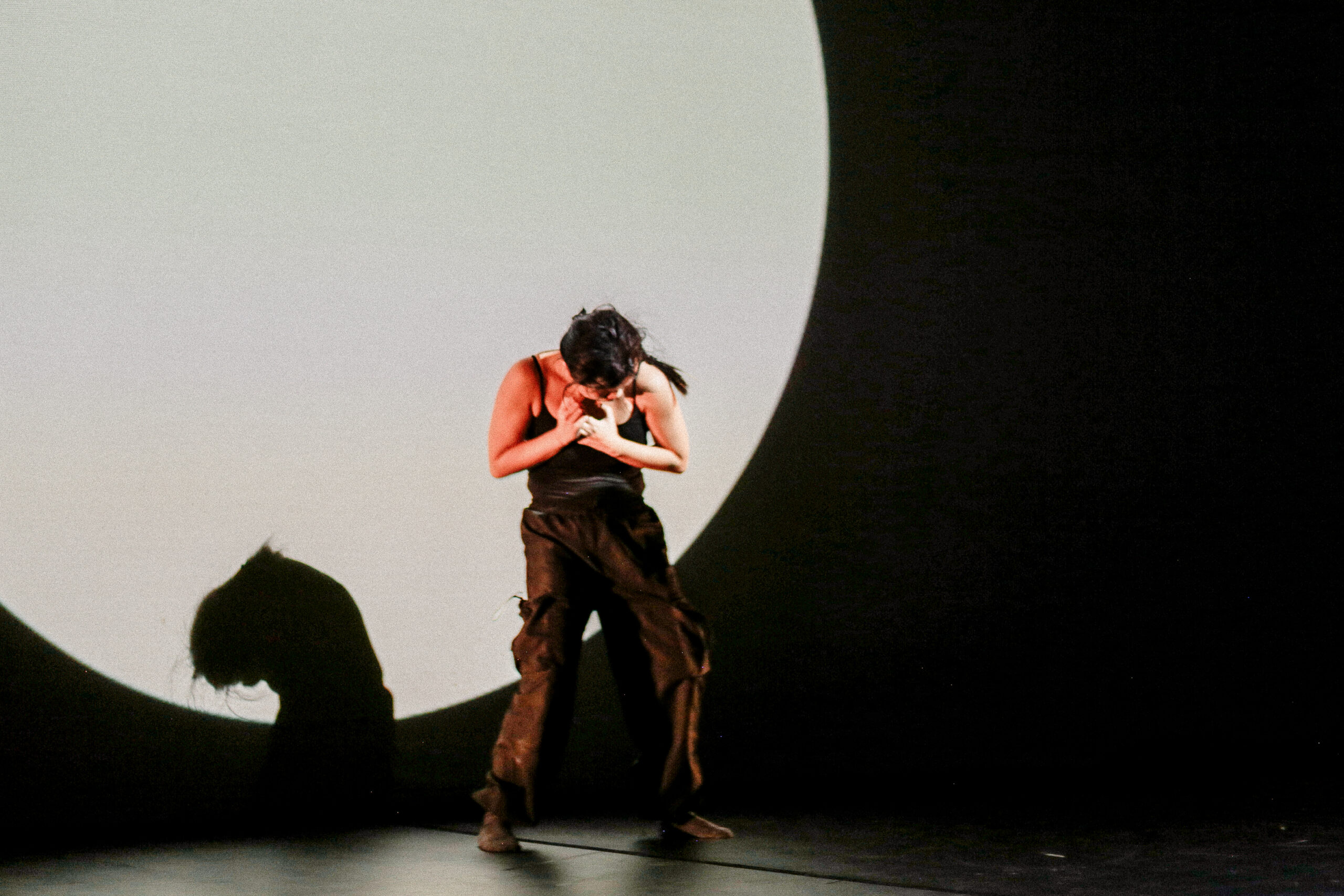 A dancer stands in bright circle of light splashed on the back wall of the theatre.