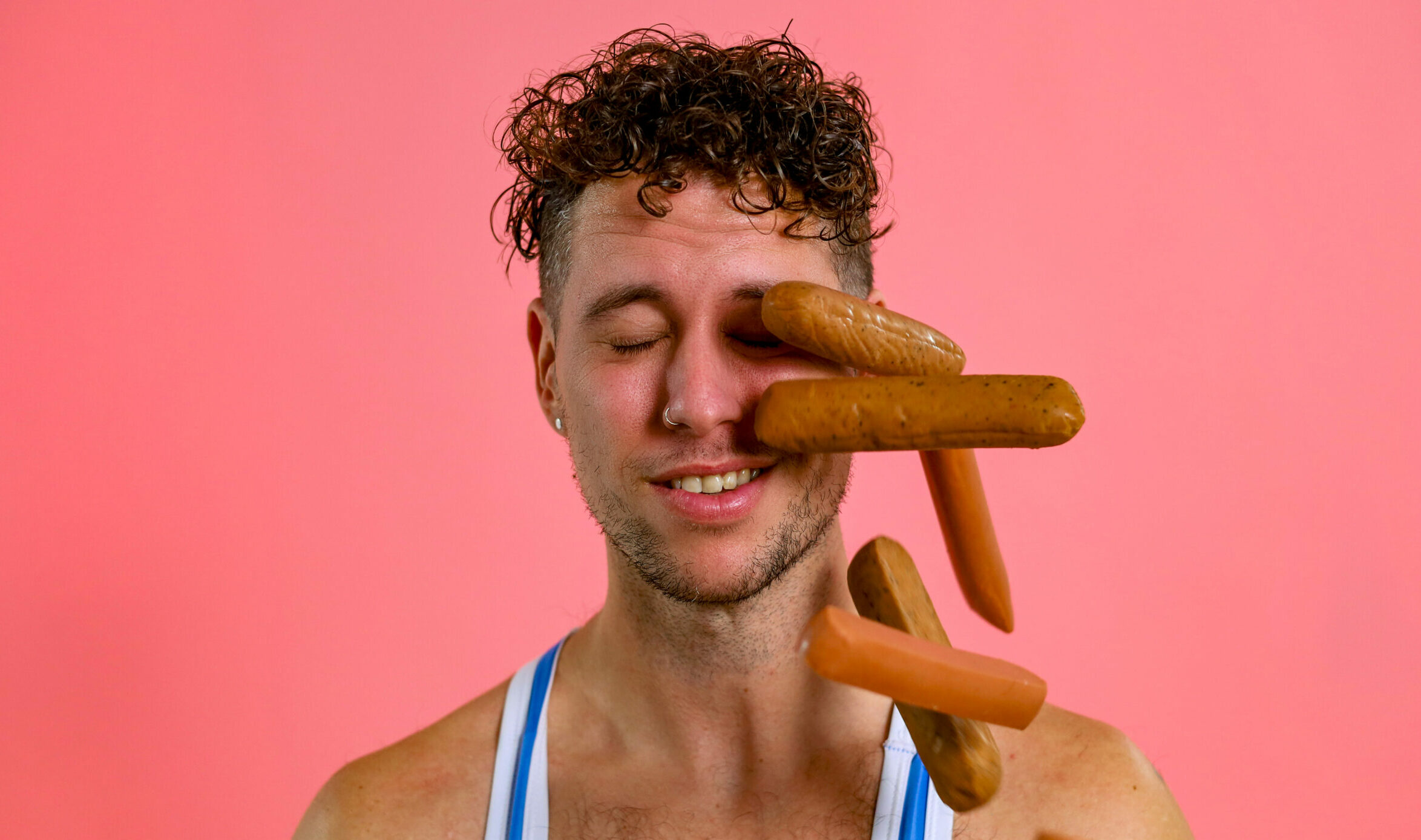 A man in a blue wrestling singlet has wieners thrown in his eye